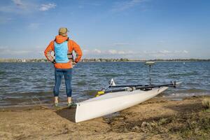 Senior male rower with his rowing shell on a beach of Boyd Lake in northern Colorado, early spring scenery photo