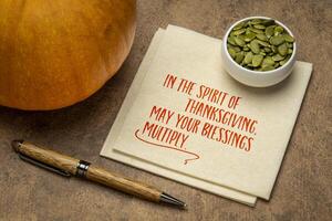 In the spirit of Thanksgiving, may your blessings multiply - text on a napkin with pumpkin, a greeting card. photo