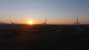 Distant wind turbines lined across fields under a setting sun, with warm light reflecting on the agricultural landscape, emphasizing renewable energy sources video
