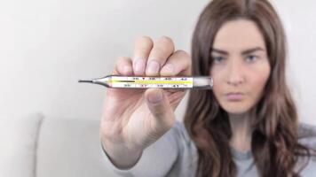 Woman shows mercury thermometer with a temperature of 37,7 C. She has a runny nose, snot flows close up animation video