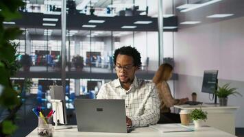 Account executive multitasking on his computer to finish business tasks and operations. African american man reviewing financial documents for company success, productivity. Camera B. video