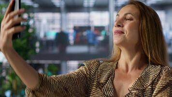 Entrepreneur takes a break from work and snaps some pictures in a corporation, working on business tasks and using her smartphone to take photos. Confident businesswoman captures selfies. Camera A. video
