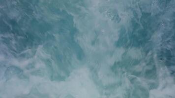 Close-up of waves and splashes with white sea foam forming patterns on surface of deep blue water. Ship trails in blue ocean video