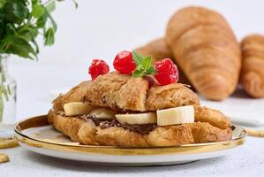 Croissant with banana pieces, chocolate paste in a round white plate photo