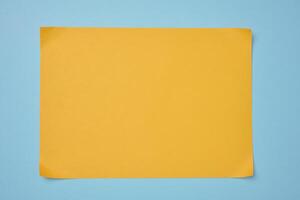 Blank yellow sheet of paper on blue background, abstract backdrop for inscription, copy space photo