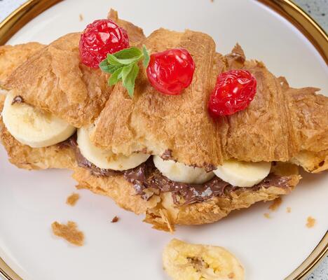 Croissant with chocolate spread and banana pieces in a white round plate on the table, breakfast
