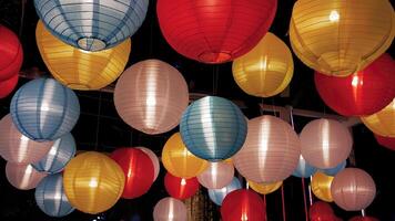 Colorful Various illuminated paper lanterns lights hanging in dark background at Thai Red Cross Fair night market, carnival season photo