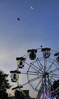 Low angle view of Ferris or Wonder wheel in silhouette shadow against twilight sky at Thai Red Cross Fair night market, amusement ride zone, carnival season photo