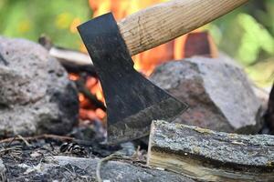 Hatchet lodged in a log of wood, situated opposite a campfire photo