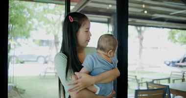 Portrait of Beautiful woman stands in a coffee shop, smiling warmly as she gently cradles a baby boy in her arms. Relaxed atmosphere add to the heartwarming moment. photo