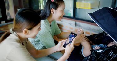 High angle view, Two women are having fun playing with little boy in a baby stroller and recording a cute on mobile phone in a coffee shop. Family enjoying happy time together photo