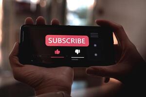 Close-up view of a woman using a smartphone to press red subscribe button on online media. Concepts of technology and following news, hot trends and new content on social media photo