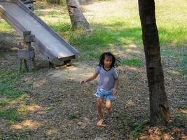 Children play outdoors on a wooden playground in a park. Happy girl playing on slide in playground in summer. photo