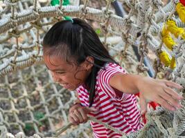 Children play outdoors on a wooden playground in a park. Happy girl playing on a rope net bridge in playground during summer. photo