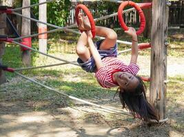 Children play outdoors on a wooden playground in a park. Happy girl playing on climbing swings in playground during summer. photo