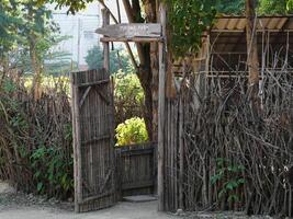 Rustic fence made with tree branches and wooden posts with a small gate leading to the entrance to a mini zoo. photo