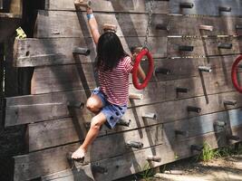 Children play outdoors on a wooden playground in a park. Happy girl playing on wooden climbing wall in playground during summer. photo