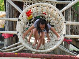 Children play outdoors on a wooden playground in a park. Happy girl playing on a rope net bridge in playground during summer. photo