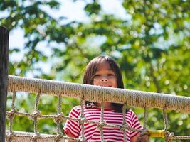 Children play outdoors on a wooden playground in a park. Happy girl playing on a rope net bridge in playground during summer. photo