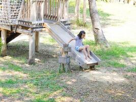 Children play outdoors on a wooden playground in a park. Happy girl playing on slide in playground in summer. photo
