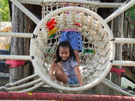 Children play outdoors on a wooden playground in a park. Happy girl playing on a rope net bridge in playground during summer. photo