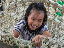 Children play outdoors on a wooden playground in a park. Happy girl playing on a rope net bridge in playground during summer. photo