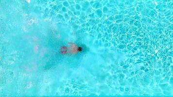 Aerial view as a man dives into the pool and swims. Slow motion video