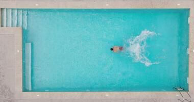 Aerial view as a man dives into the pool and swims. Slow motion video