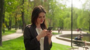 Thoughtful woman walking in park using mobile phone smartphone gadget texting online chat connection smiling happy sms thinking technology web social networks stroll typing city outside female girl video