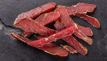 macro photo of dried sliced lamb basturma on black marble surface top view