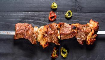 macro photo of lamb shish kebab on skewers on a black wooden surface top view