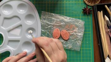 Female artist mixes white acrylic paint with water in palette with brush to paint clay figures with faces. Tools for modeling on table. Handmade, craft and leisure at home on quarantine. video