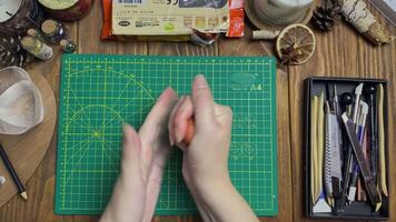 Women's hands knead piece of clay, dip it in water and again crumple it. Modeling tools, jars, decor on wooden table. Potter's workshop. Handmade and craft. video