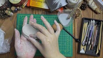 Master with wet hands makes egg mold out of white clay. Tools for modeling and design of ceramic souvenirs. Hobbies, handmade and crafts. Water, stationery knife, sticks on wooden table. video