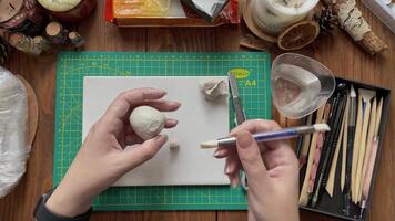 Master make form of clay with wet hands and rubber brush. Tools for modeling and design of ceramic souvenirs. Stationery knife, cup with water and sticks on wooden table. Hobby handmade and crafts. video