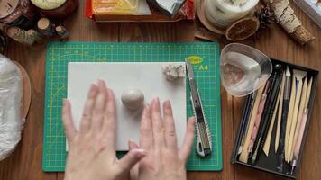Women's hands make form of clay and wetting it with water. Tools for modeling and design of ceramic souvenirs. Hobbies, handmade and crafts. Stationery knife, sticks on wooden table. video