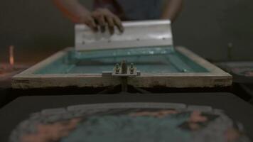 textile factory process, man pushing squeegee inside a printing frame, textile and cloths printing process video