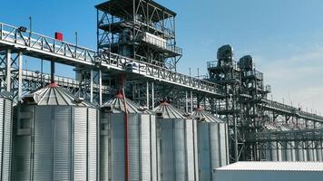 Industrial grain silos with metal structures against blue sky. A large-scale industrial grain storage facility with multiple metal silos connected by complex structures and pipelines. video