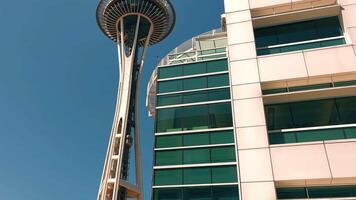 Seattle Washington 10.09.2024 Space Needle towering over modern glass building. The iconic Space Needle is seen towering over a modern glass building against a clear blue sky. video
