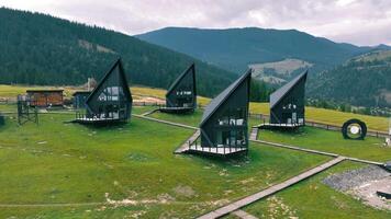 Aerial Modern A-Frame Cabins on Grassy Hillside. A group of modern black A-frame cabins with sharp architectural lines, video