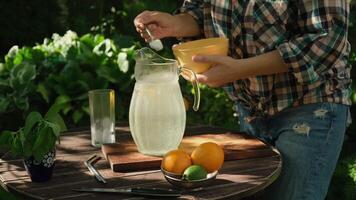 Summer vibes. Making homemade lemonade outdoors, refreshing summer drink. Hands adding sugar with spoon into jug of lemonade. video