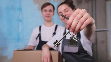 Own home. Mortgage relocation concept. Happy couple holding key from new first house. Family celebrating moving day. Husband wife customers buyers purchase real estate hold moving box showing keys video