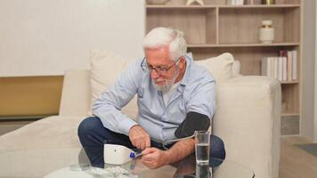 Hypertension problem in senior age. Old man measuring blood pressure with tonometer at home. Senior man have health problem making self checkup. Headache treatment of hypertension hypotension video