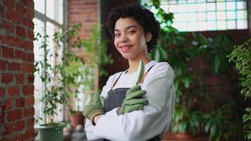 Running of own business. African woman florist wearing apron in botanical store with green plants. Happy small business owner working at flower shop smiling surrounded by plants Small business video