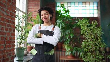 Running of own business. African woman florist wearing apron in botanical store with green plants. Happy small business owner working at flower shop smiling surrounded by plants Small business video