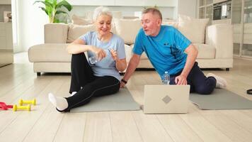 Yoga mindfulness water. Senior adult mature couple drinking water after practicing yoga with online lessons in laptop. Old wife husband drink water before workout. Family doing sports exercise at home video
