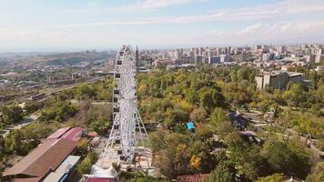 Yerevan, Armenia - 19th october, 2024- Aerial fast motion circular view ferris wheel in Victory Park ir with cityscape and buildings of Yerevan. Sunny autumn day carousels day out things to do concept video