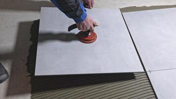 Tiler worker placing or tiling gray ceramic tile in the position over adhesive glue with lash tile leveling system, renovation or recontruction, concept of building video