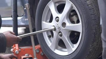 A man is kneeling down next to a car with a jack and a tire iron. He is fixing the tire. video