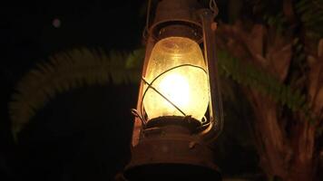 An oil lamp lantern hanging from a tree with a light inside. The lantern is old and rusted. video